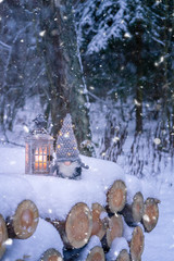 Naklejka premium Toy gnome with a candle sits on logs in a snowy forest at dusk