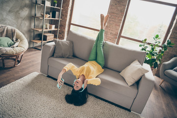 Full length photo of cheerful positive bare-foot girl have free time sit divan upside down listen...