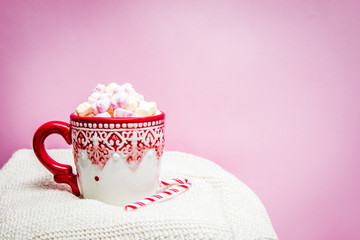 Red Christmas mug with marshmallows, sugar cane on a cozy sweaters and pink background 