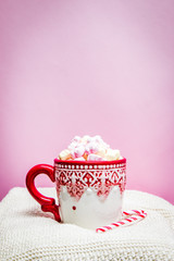 Red Christmas mug with marshmallows, sugar cane on a cozy sweaters and pink background 