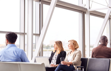 Businesswomen Sitting In Airport Departure Working On Laptop And Drinking Coffee