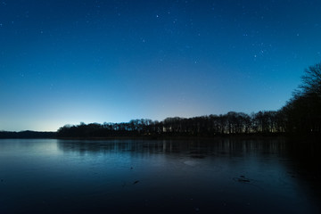 Fototapeta na wymiar Sterne über dem See und Wald im Winter