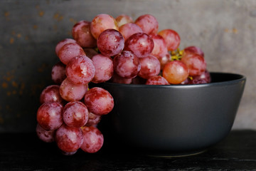 Tasty fresh pink grapes in bowl on dark rustic background.