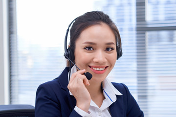 Portrait of happy smiling female customer support phone operator at workplace. Asian