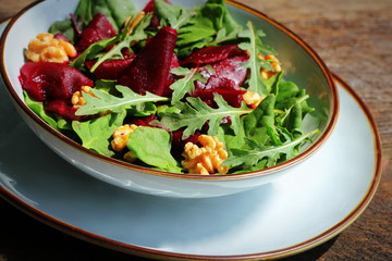 Healthy Beet Salad with fresh sweet baby spinach, arugula, nuts on wooden background
