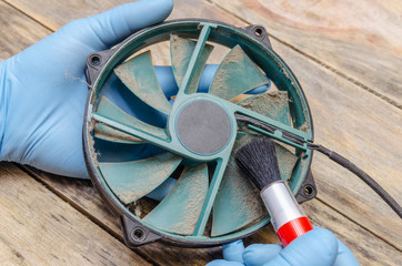 Cleaning the dusty green cooler from the computer with a brush and vacuum cleaner on a wooden table close-up. concept of scrapers parts of the computer