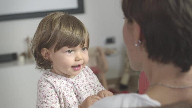 Portrait of cute little one year old girl reading playing learning and looking at a book on the lap of her mother at home. Shot in 6k, cine lens.