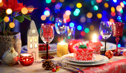 Beautiful table setting for Christmas party or New Year celebration at home. Cozy room with a fireplace and Christmas tree in a background.