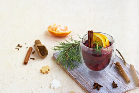 Mulled wine, heated red wine with various spices, slices of orange and apple in a glass goblet on a wooden board on a light concrete background. Christmas and New Year.