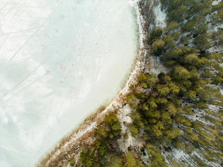 Beautiful aerial view of ice covered Balzis lake. Snowy pine forests surrounding a small lake. Scenic winter landscape near Vilnius, Lithuania.