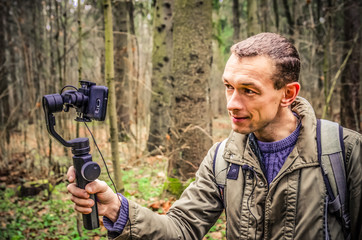 male blogger films himself in the woods on a mobile phone camera and gimbal, smiling and waving at the camera. The concept of blogging, Internet, information
