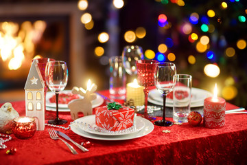 Beautiful table setting for Christmas party or New Year celebration at home. Cozy room with a fireplace and Christmas tree in a background.