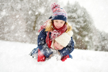 Two adorable young girls having fun together in beautiful winter park. Cute sisters playing in a snow.