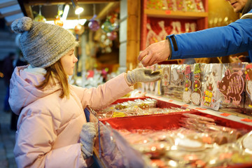 Cute young girl choosing sweets on traditional Christmas market in Riga, Latvia. Kid buying candy...