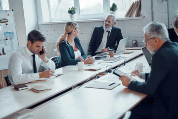 Coworkers in elegant formalwear using modern technologies while working in the office