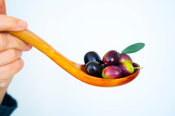 A woman handful of Mediterranean olives on a wooden spoon on isolated white background