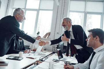 Modern businessmen shaking hands while working together with their team in the office