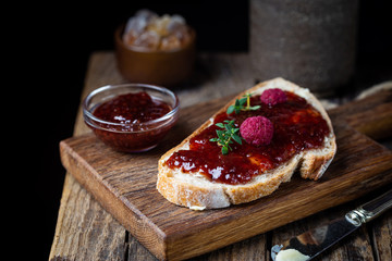 Toasted bread with sweet raspberry jam for breakfast on dark wooden background