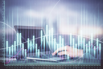 Double exposure of man's hands writing notes with laptop of stock market with forex graph background. Top View. Concept of research and trading.