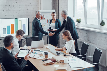 Confident businessmen shaking hands and smiling while working together with colleagues in the board room