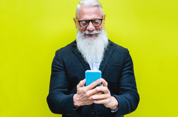 Happy senior man using smartphone app with fluorescent color in background - Hipster old guy having fun with technology - Tech and joyful elderly concept - Focus on his face