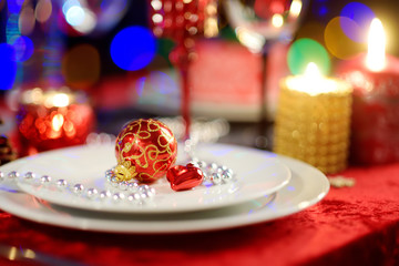 Beautiful table setting for Christmas party or New Year celebration at home. Cozy room with a fireplace and Christmas tree in a background.