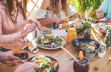 Hands view of young people eating brunch and drinking smoothies bowl with ecological straws in trendy bar restaurant - Healthy lifestyle, food trends concept - Focus on left woman hand, dish - obrazy, fototapety, plakaty