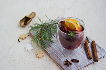 Mulled wine, heated red wine with various spices, slices of orange and apple in a glass goblet on a wooden board on a light concrete background. Christmas and New Year.