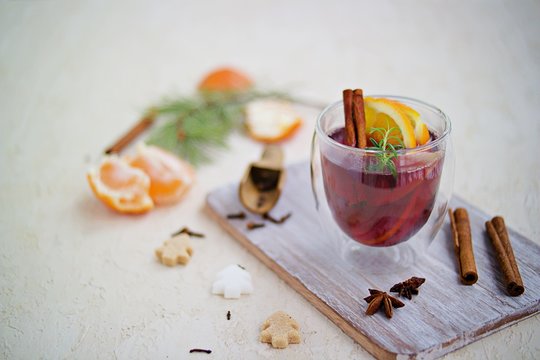 Mulled wine, heated red wine with various spices, slices of orange and apple in a glass goblet on a wooden board on a light concrete background. Christmas and New Year.