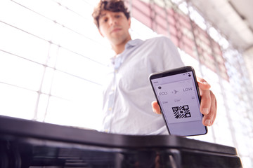 Male Passenger In Airport Departure Lounge Scanning Digital Boarding Pass On Smart Phone