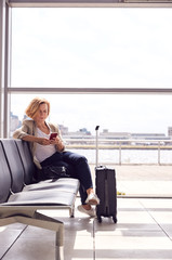 Mature Businesswoman Sitting In Airport Departure Lounge Using Mobile Phone