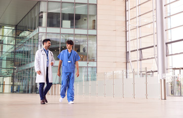 Male Medical Staff Talking As They Walk Through Lobby Of Modern Hospital Building