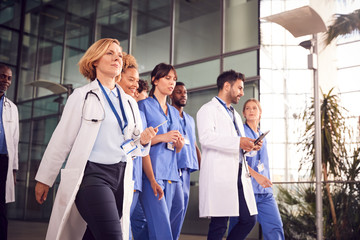 Medical Team Walking Through Lobby Of Modern Hospital Building - Powered by Adobe