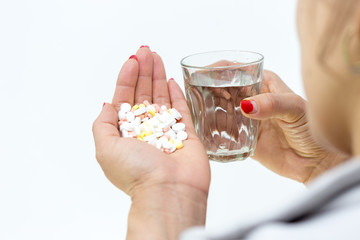in the girl’s hand a lot of pills and a glass of water on a white background