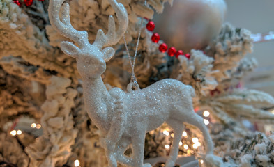White reindeer figure decoration on Christmas tree with red pearls, decorative balls and cozy yellow lights