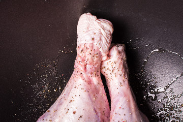 Delicate raw turkey legs sprinkled with salt and pepper in large cauldron for roasting in oven.