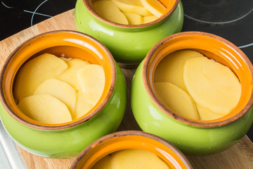 Sliced fresh potatoes lay in ceramic pot for cooking in oven.