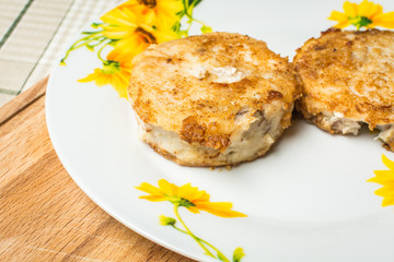 Fried round hake fish fillets in plate on kitchen table.