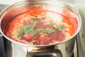 Red soup borscht cooked in large pan on stove.