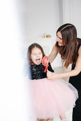 Young mother and fanny daughter with red candy in evening dresses on background of Christmas tree