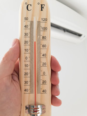 Thermometer and temperature measuring with modern air condition unit on a white wall inside the...