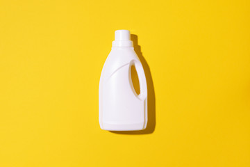 White plastic bottle of cleaning product, household chemicals or liquid laundry detergent on yellow...