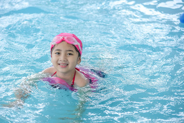 Fototapeta na wymiar Happy girl wear pink swimsuit & swimming in a pool