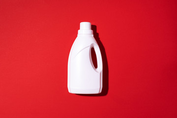 White plastic bottle of cleaning product, household chemicals or liquid laundry detergent on red...
