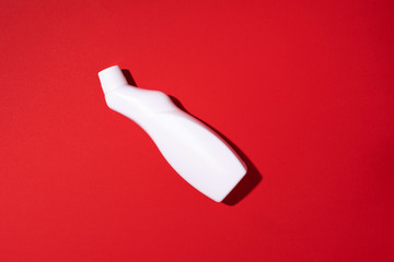 White plastic bottle of cleaning product, household chemicals or liquid laundry detergent on red background. Top view. Flat lay. Copy space. Detergent bottle