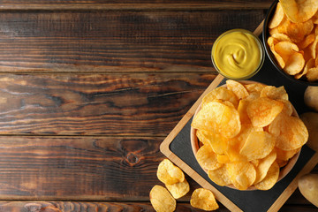 Potato chips. Beer snacks, sauce, potato on cutting board, on wooden background, space for text. Top view