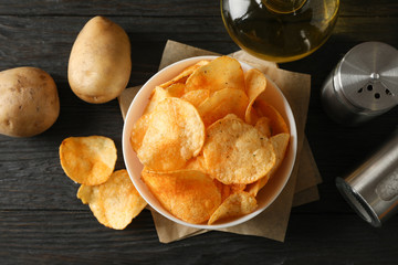 Potato chips in a bowl on craft paper. Potato, spice, olive oil on wooden background, closeup. Top view