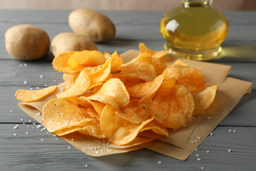 Potato chips on craft paper, sault, oliv oil, potato on gray wooden background, space for text. Closeup