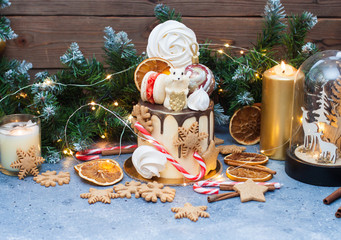 Cake decorated with melted chocolate, candy cane, meringue, christmas tree balls, chocolate mouse, macaroons, christmas gingerbread cookies and dried oranges. 