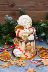 Cake decorated with melted chocolate, candy cane, meringue, christmas tree balls, chocolate mouse, macaroons, christmas gingerbread cookies and dried oranges. 